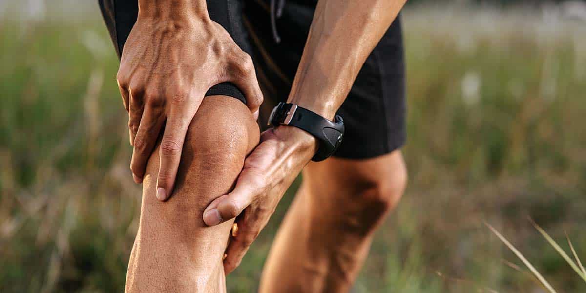 Detalhe de mãos de homem pegando no joelho com dor de gota - site Dr. Marcelo Correa - Reumatologista em Belém - PA